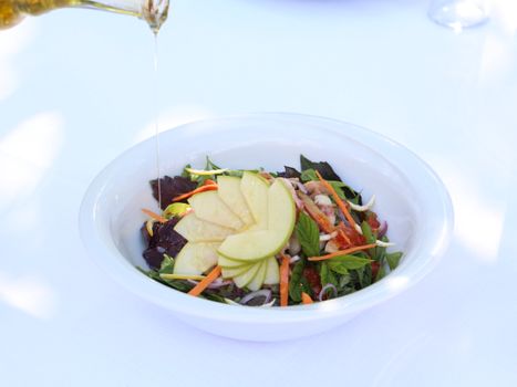 Colorful apple salad in a white bowl with olive oil drizzling, bursting with fresh veggies.