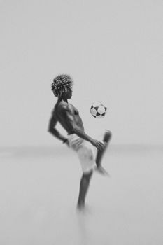 Shirtless man skillfully juggling a soccer ball on a Brazilian beach.