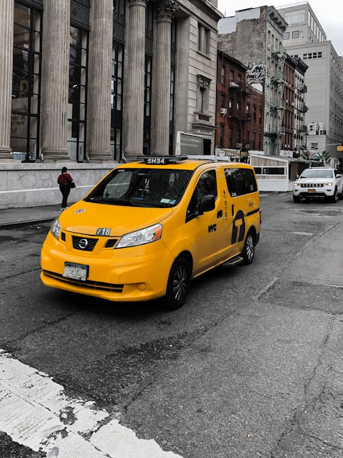 Free A Yellow Taxi Moving on the Road Near the Concrete Buildings Stock Photo