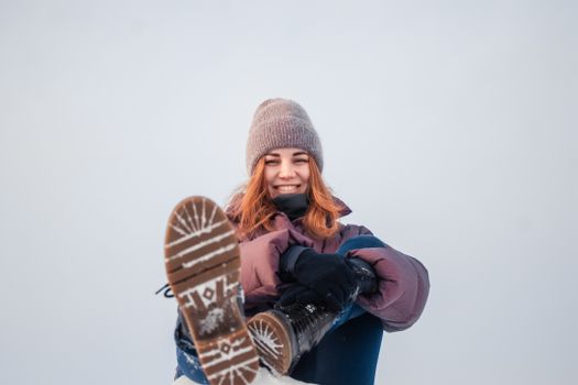A redhead woman in winter attire smiling while sitting outdoors in the snow.
