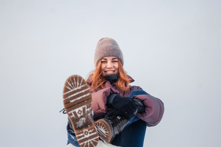 Redhead Girl In Warm Clothing Sitting On Snow