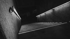 这是一张黑白照片，光影变幻莫测，照亮了一段带有扶手的楼梯，营造出深邃而神秘的氛围