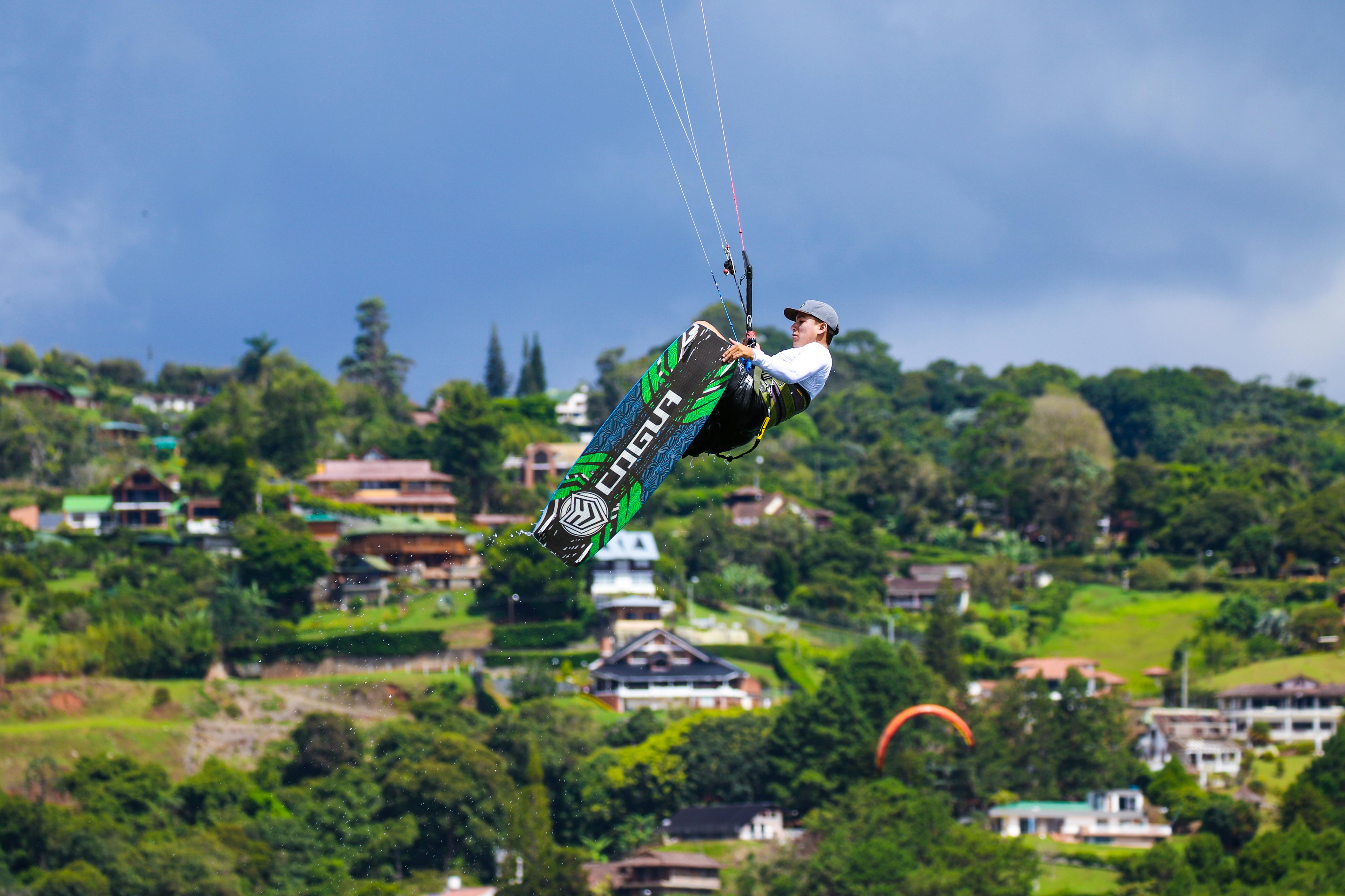 Kiteboarder performing tricks over lush landscape, showcasing extreme sport in a vibrant setting.
