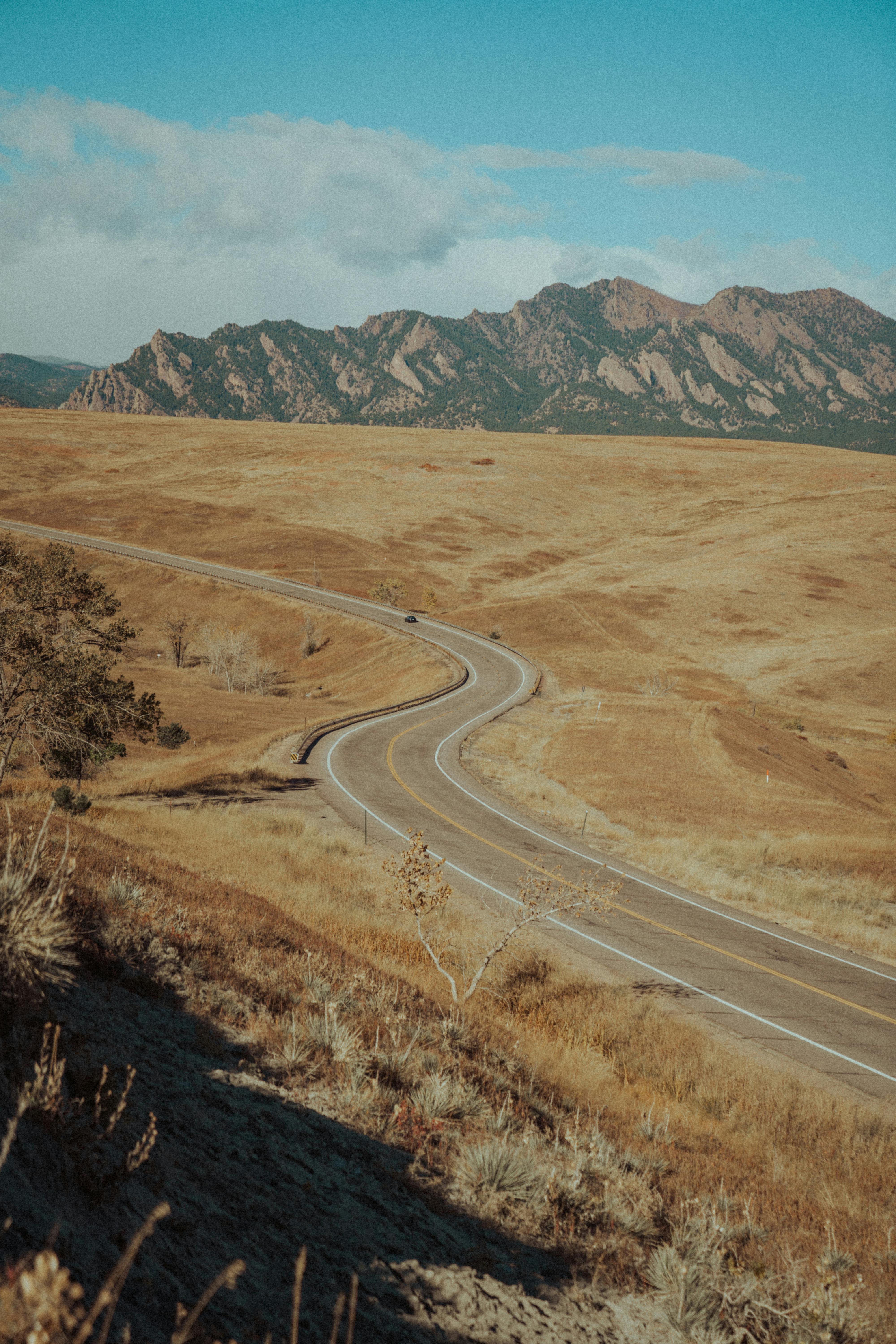 A winding road through a golden, barren landscape with distant mountains under a blue sky.