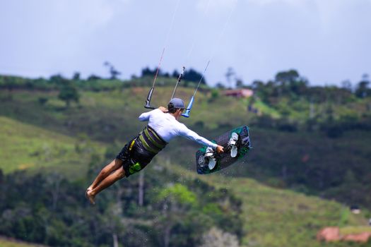 Kiteboarder performs an aerial maneuver over lush green hills on a sunny day.