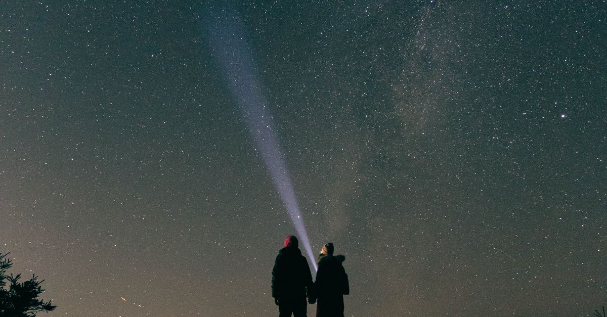 Rüyada Sevgiliyle Yıldızların Altında Olmak - Rüya Tabiri ve Anlamı - Silhouette of a couple under a starry night sky using flashlights with Milky Way visible.
