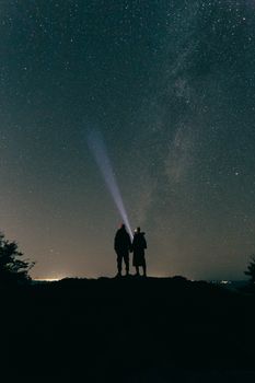 Silhouette of a couple under a starry night sky using flashlights with Milky Way visible.