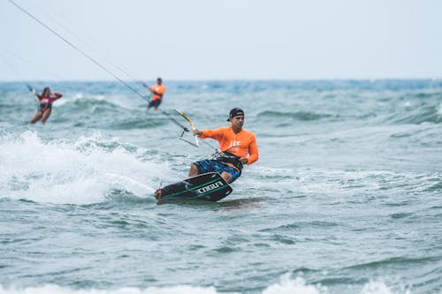 Free Man in Orange Shirt Riding on Black Board on Sea Stock Photo