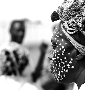 Artistic black and white portrait of an African woman adorned with a traditional beaded headdress and face paint.