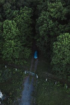 A drone captures a blue car driving an unpaved forest road in Nikoleavka, Russia.