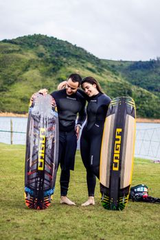 A couple in wetsuits holding kiteboards in a scenic outdoor location.