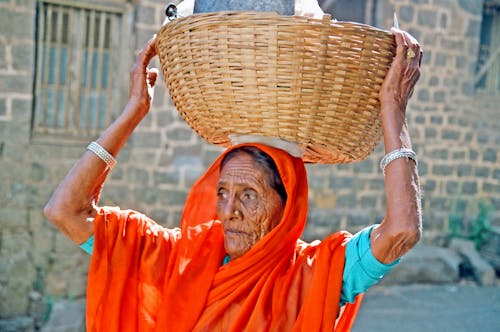 A Woman in Orange Scarf Carrying a Woven Basket on Her Head