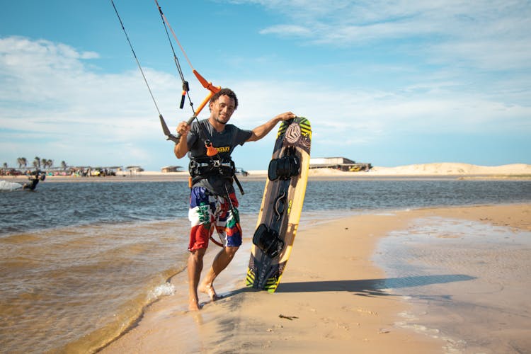 Man Standing On A Beach Holding A Surfboard And Cords Of A Kite