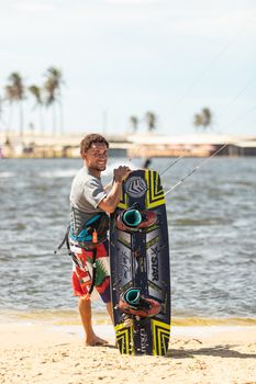 Man enjoying a sunny day by the water, holding a kiteboard with tropical scenery.