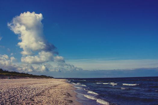 A serene beach scene with dramatic clouds and gentle waves under a vivid blue sky.