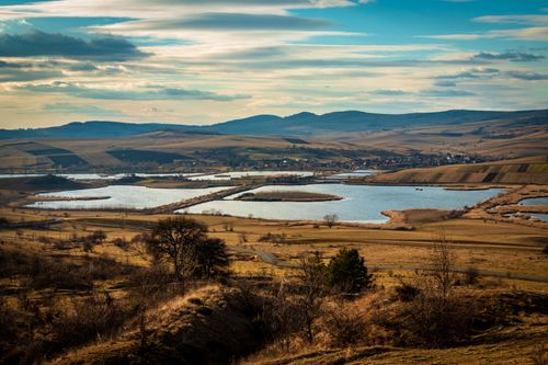 Free A breathtaking aerial view of a serene rural landscape with fish ponds and rolling hills under a dynamic sky. Stock Photo