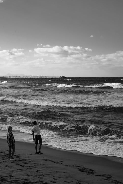 Black and White Photo of Man and Woman Standing on Shore