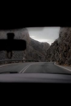 View from a car's interior driving through a canyon road with steep cliffs.