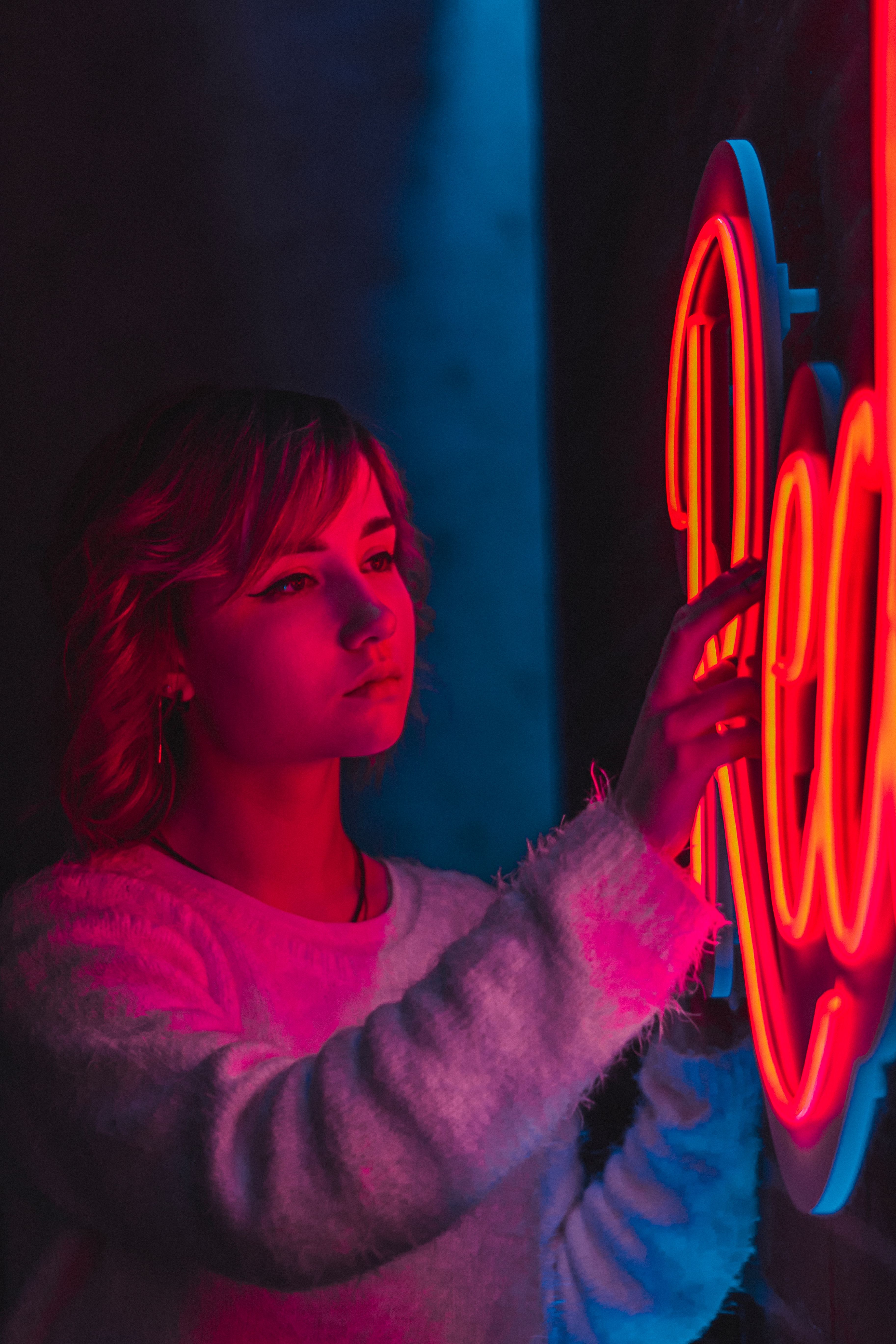 Portrait of a young woman standing next to a vibrant neon sign, creating a moody atmosphere.