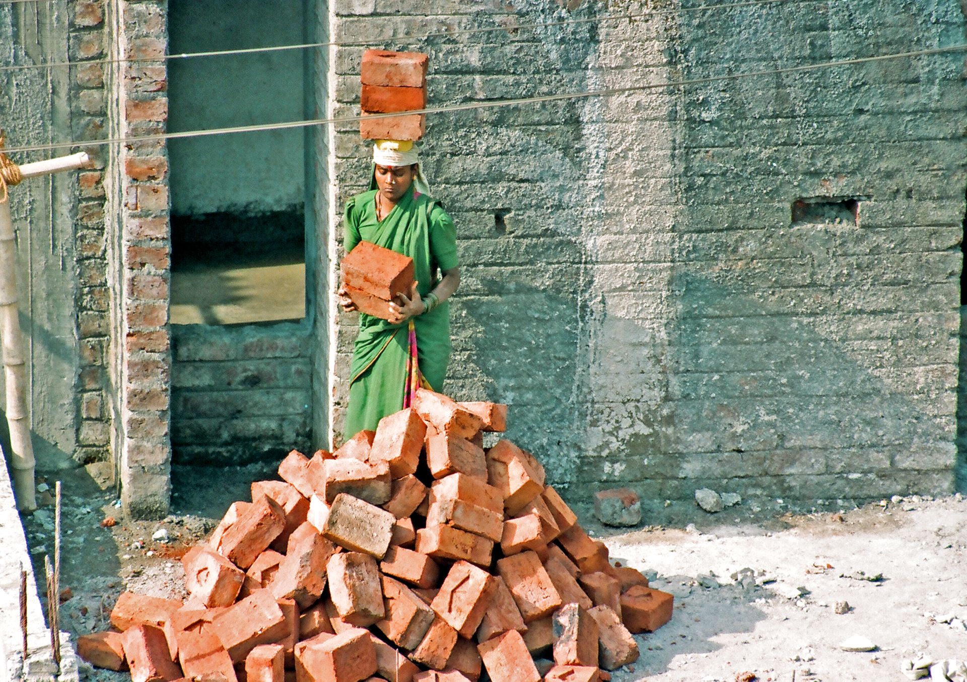A hardworking woman in India carrying red bricks at an outdoor construction site.