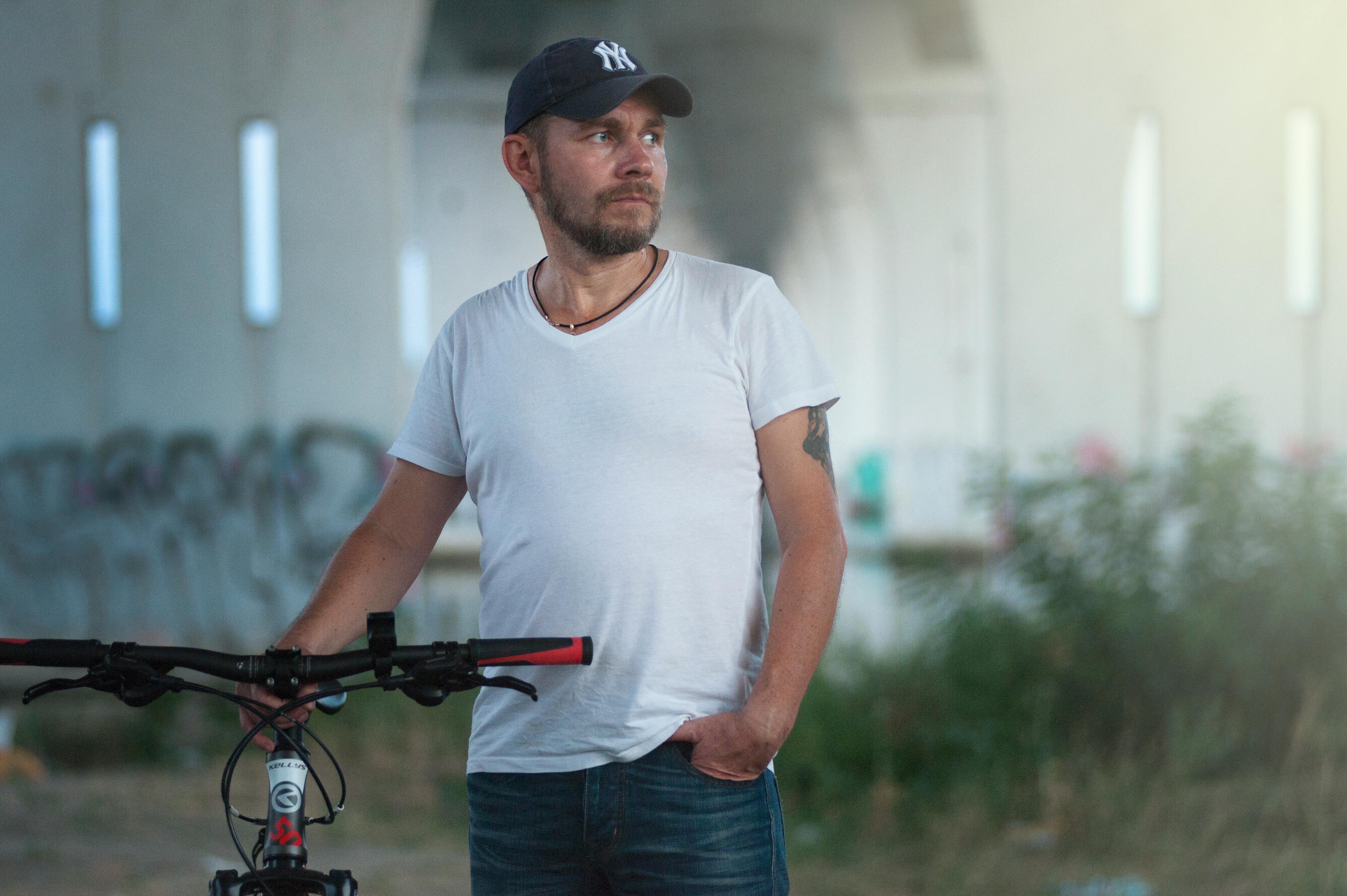 白天，一名戴着帽子、穿着休闲装的男子在城市的一座桥下骑自行车