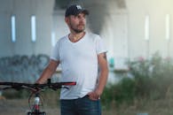 白天，一名戴着帽子、穿着休闲装的男子在城市的一座桥下骑自行车