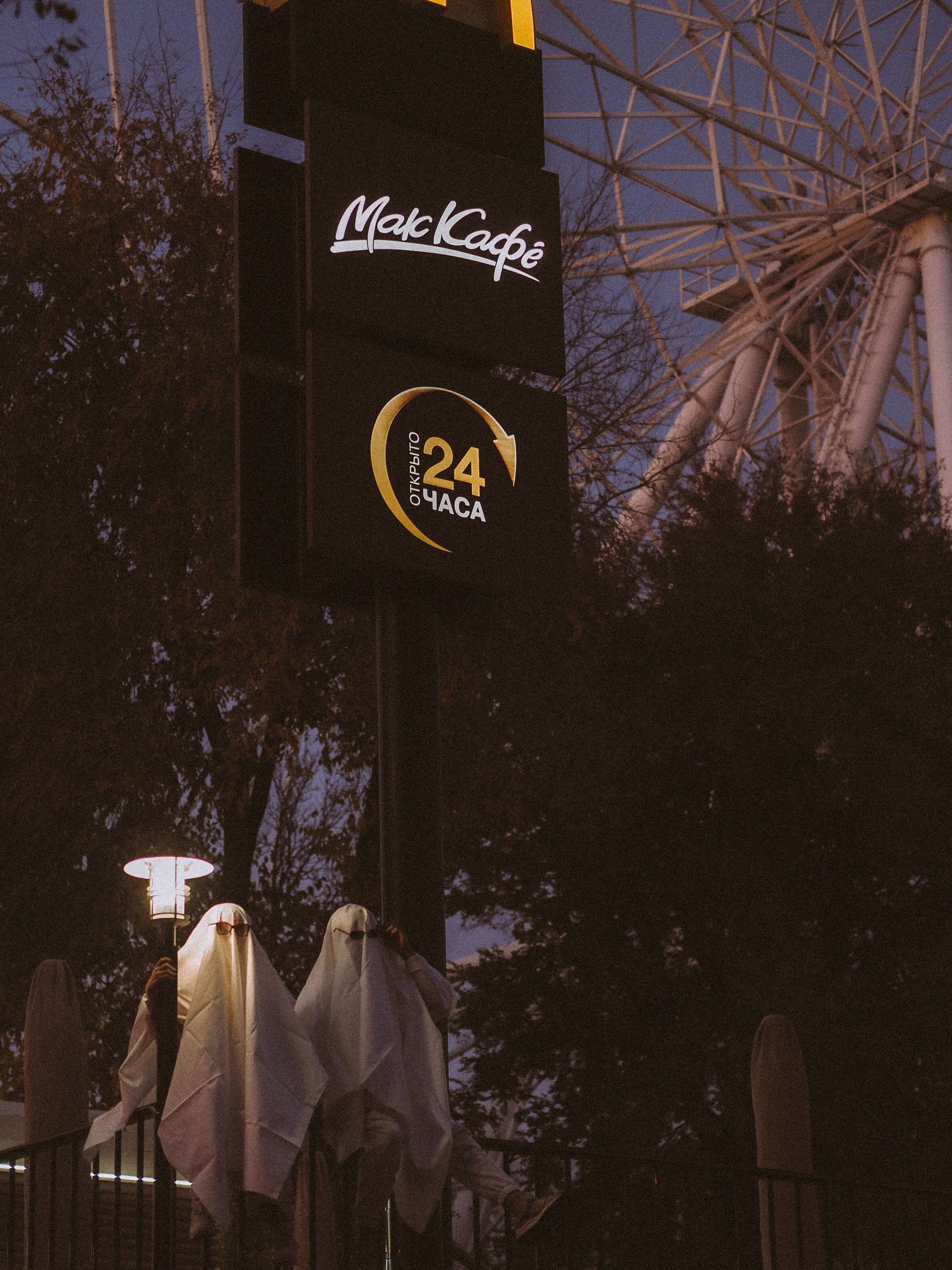 Two people in ghost costumes near a McCafé sign during twilight, creating a spooky Halloween atmosphere.