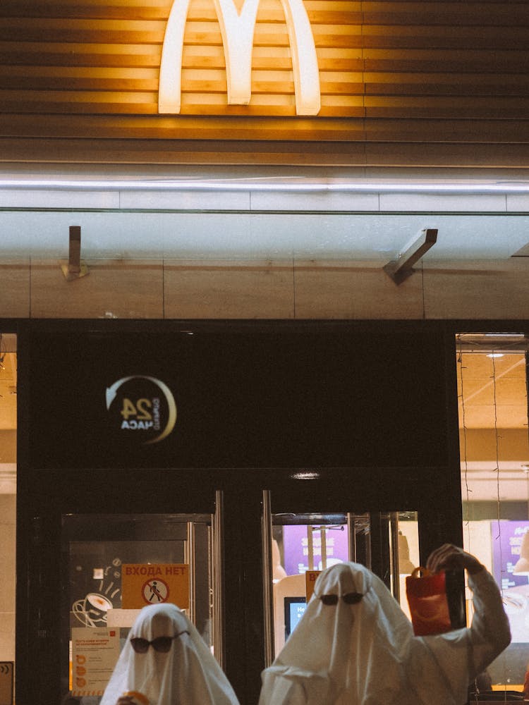 People Covered With White Blankets Standing In Front Of McDonald's
