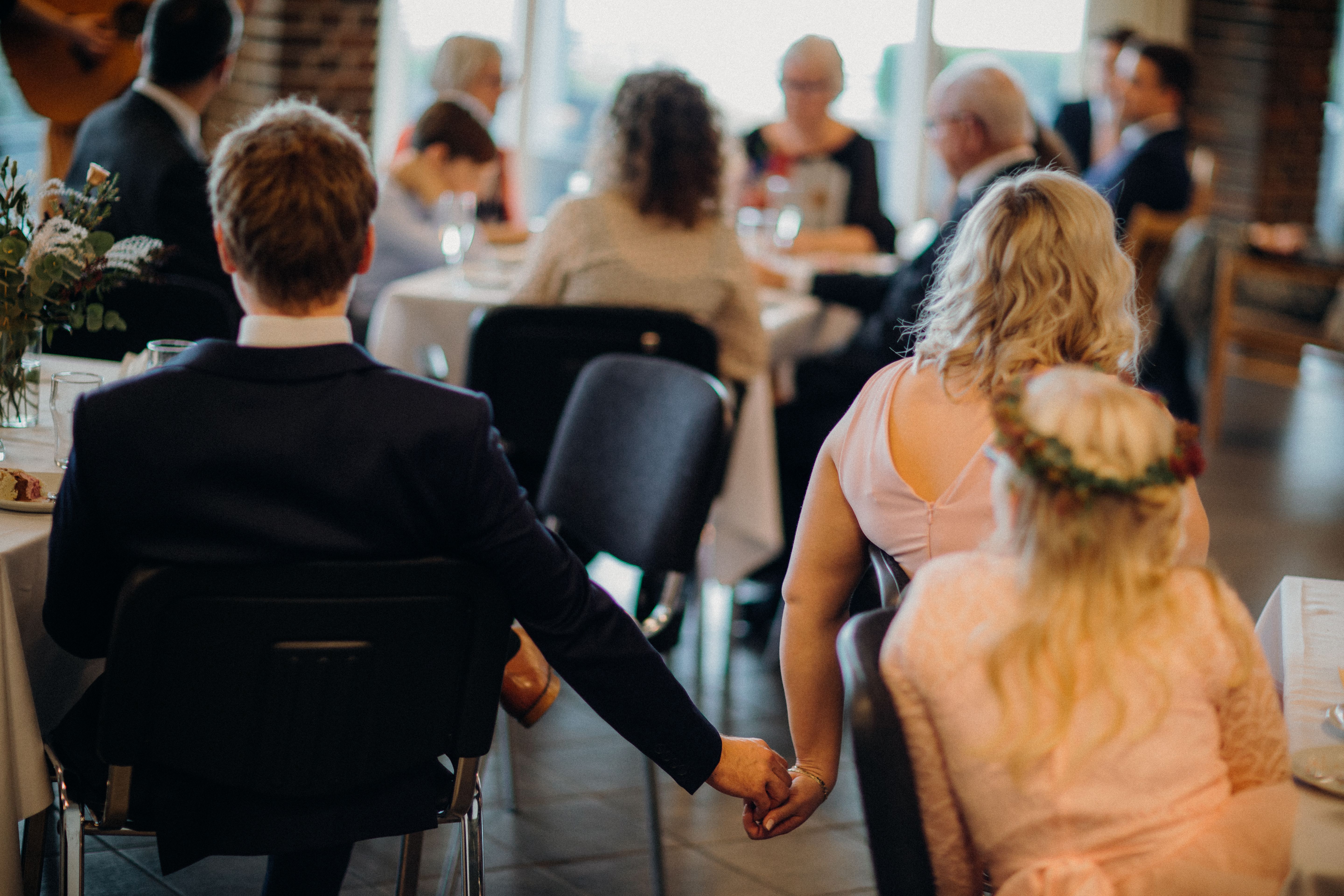 Elegant scene of a couple holding hands at a wedding reception, captured from behind.