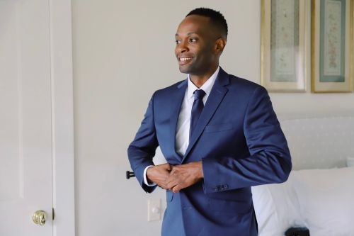 Free Smiling man in a blue suit buttoning his jacket indoors. Stock Photo