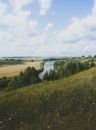 Green Grass Field Near River Under White Clouds and Blue Sky