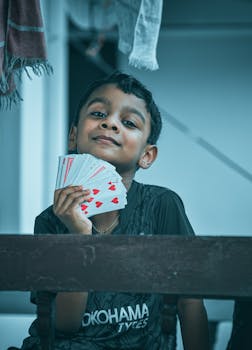 Young boy cheerfully displaying a hand of playing cards, capturing a playful moment.