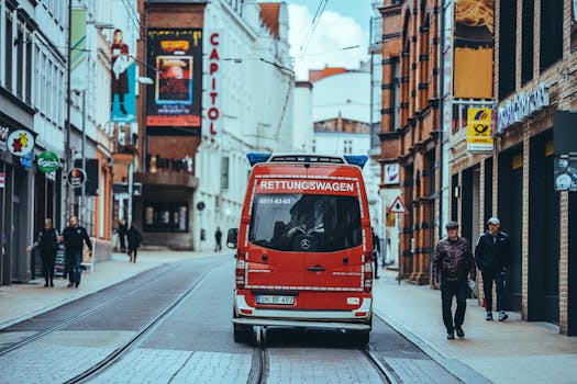 Ambulance driving down an urban street, surrounded by pedestrians and buildings.