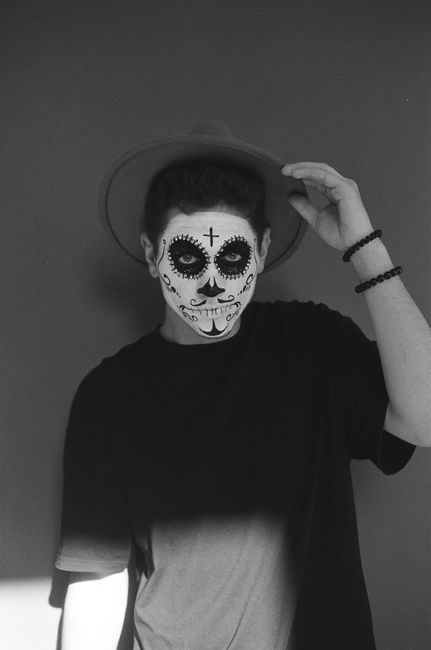 Artistic black and white portrait of a man with Day of the Dead face paint and a hat.