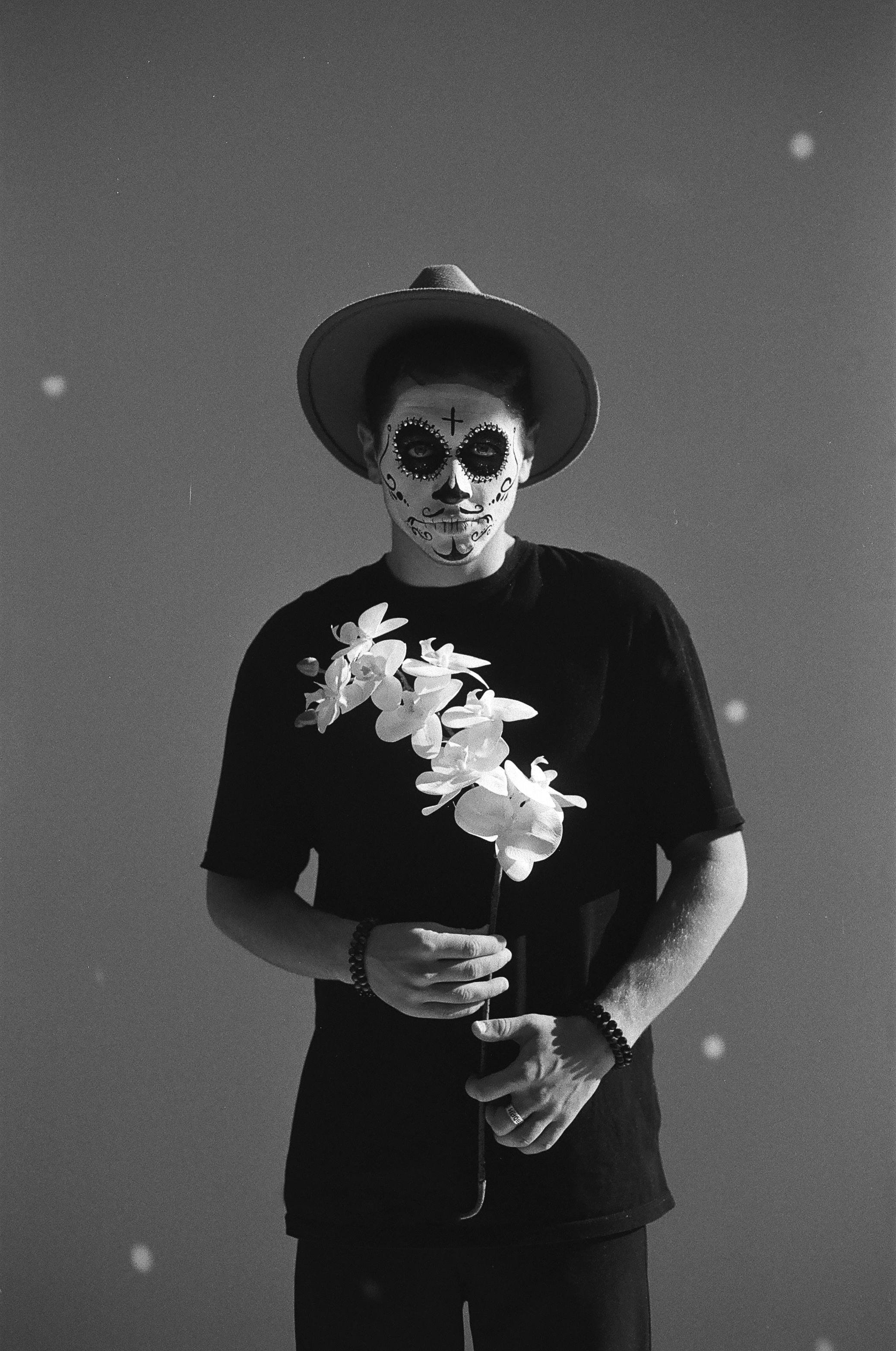 Black and white photo of a man with Day of the Dead makeup holding white flowers.