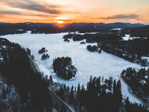 Free A stunning aerial view of a frozen lake surrounded by forests at sunset, capturing the serene winter landscape. Stock Photo