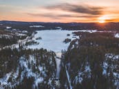 日出时分，白雪皑皑的森林与冰封湖泊的鸟瞰景象令人惊叹，捕捉了冬日宁静之美