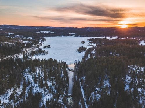 Free A breathtaking aerial view of a snow-covered forest and frozen lake at sunrise, capturing the serene beauty of winter. Stock Photo
