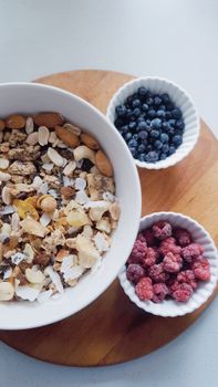Top view of a breakfast setup with granola, almonds, blueberries, and raspberries in bowls.