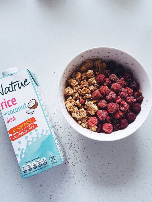 A white bowl filled with crunchy golden-brown gluten-free cereal clusters, with a small pitcher of milk beside it and a few clusters scattered on the counter.