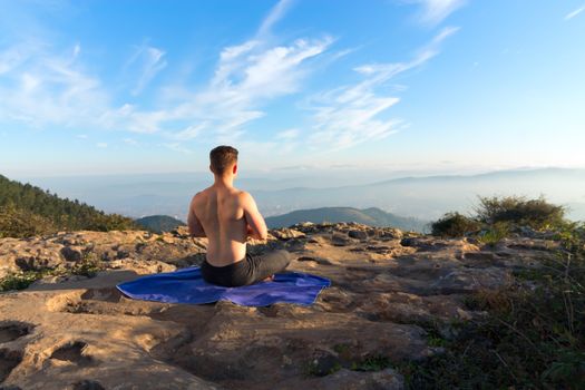 Shirtless man meditating outdoors on a mountain top, enjoying a panoramic view.