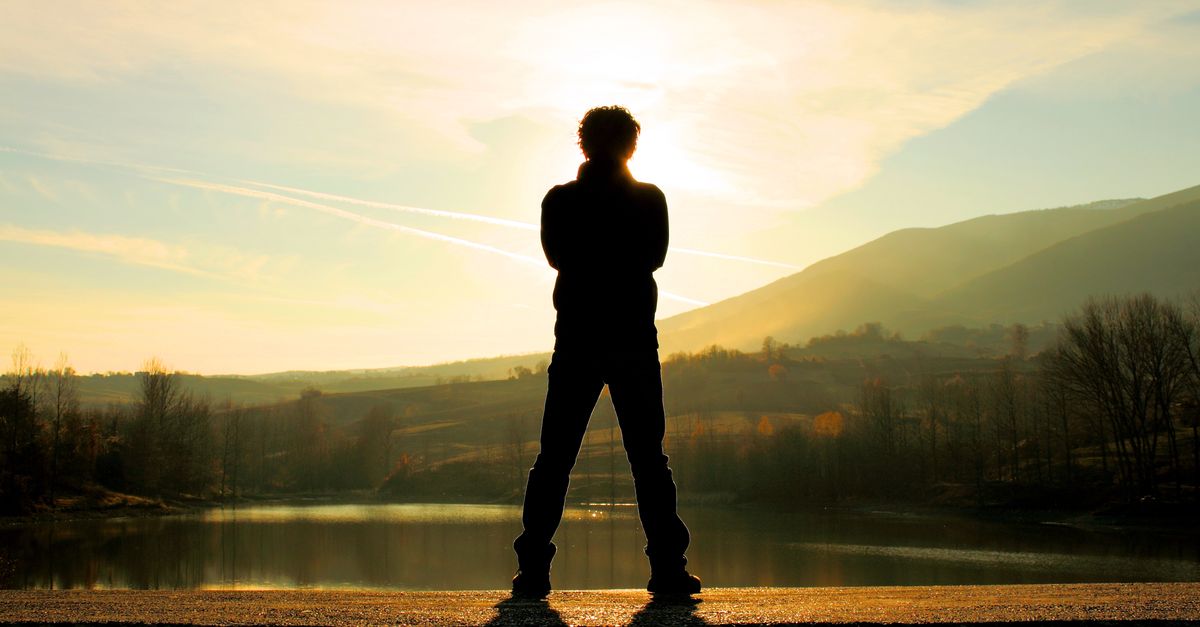 A lone figure stands settled at the water's edge at dusk — present, unhurried, taking up his own space.