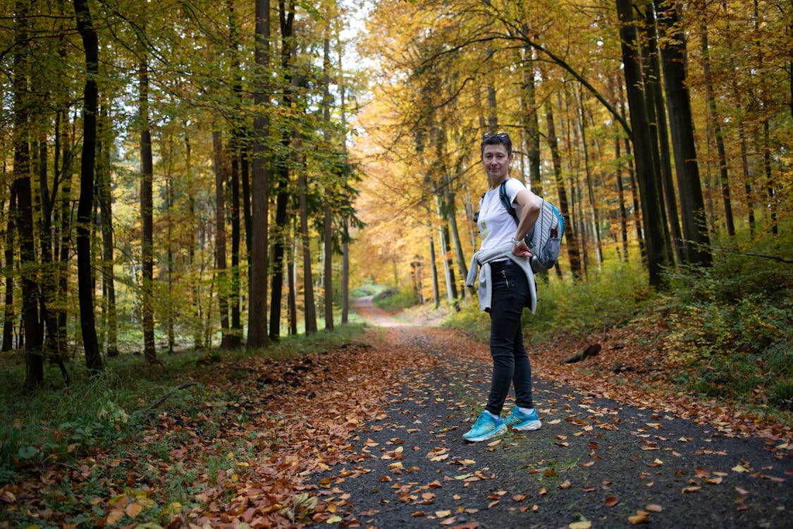 Free Woman in White Long Sleeve Shirt and Black Pants Standing on Forest Stock Photo