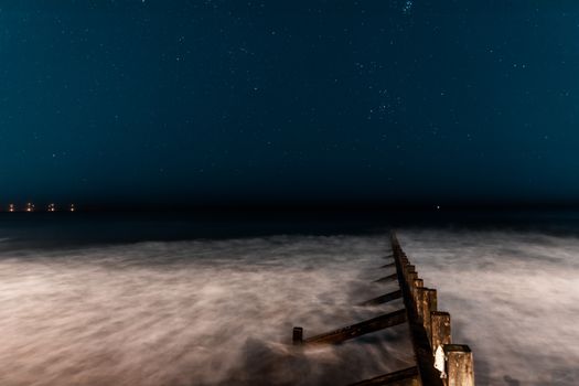 A serene night view of the Scottish coast with a wooden groyne and starry sky.