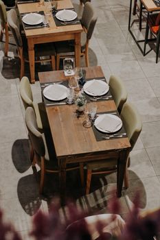 Top view of a neatly set restaurant table with ceramic plates, wine glasses, and wooden chairs.