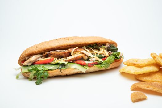 A tasty chicken baguette with fresh vegetables and side potato chips on a white background.