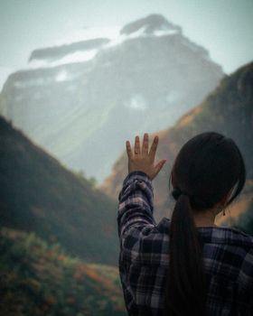 A woman in a plaid shirt reaches out towards a misty mountain in Dagestan, Russia.