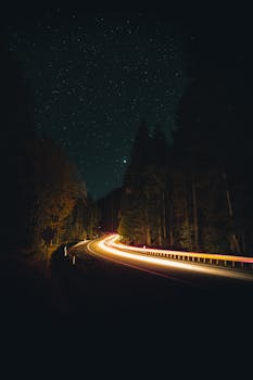 Beautiful long exposure of a curving road at night under a starry sky with glowing light trails.