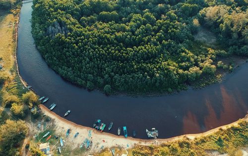 Free A tranquil aerial view of a river winding through lush forests with boats along the shore. Stock Photo