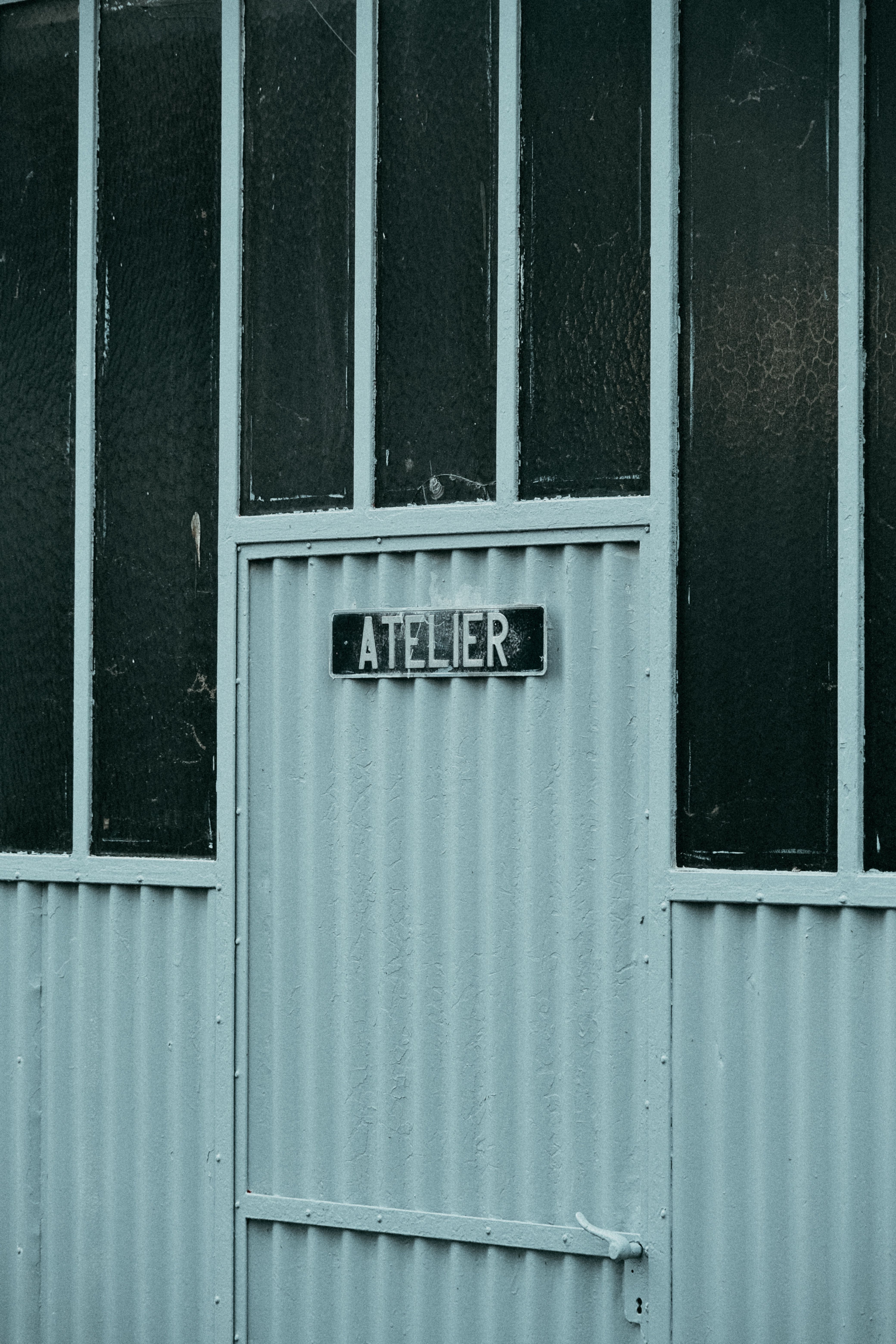 Close-up of a vintage atelier facade with textured green panels and a sign on the door.